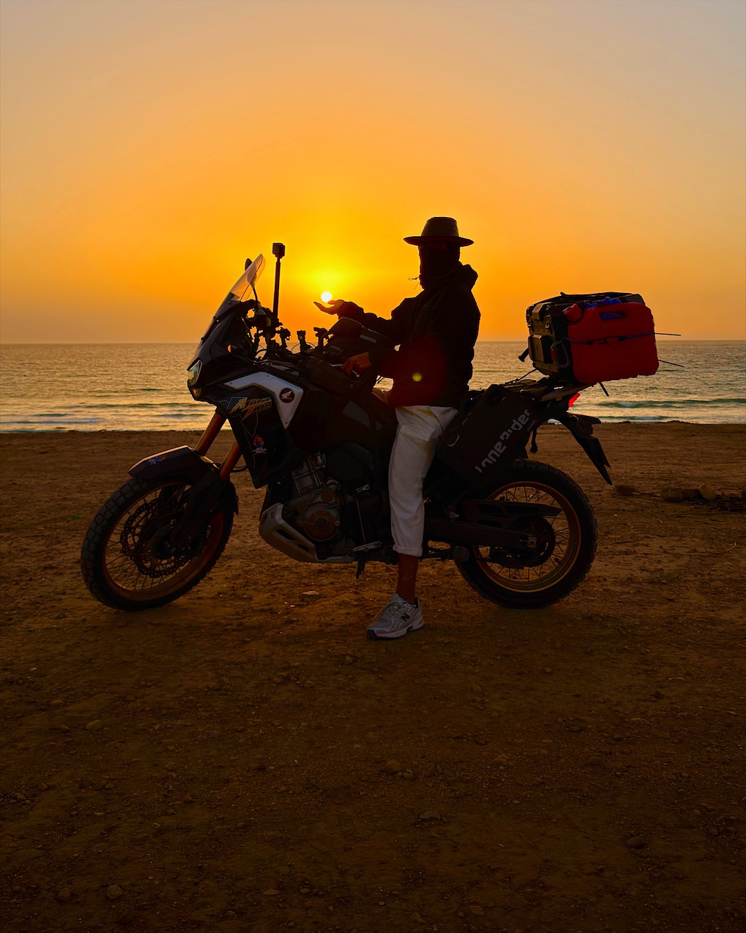 Lachetontel sur son Africa Twin, en contre-jour face au soleil couchant sur la mer